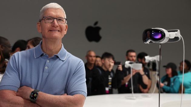 In this June 5, 2023, file photo, Apple CEO Tim Cook stands next to the new Apple Vision Pro headset, displayed during the Apple Worldwide Developers Conference in Cupertino, Calif. -- Justin Sullivan/Getty Images, FILE