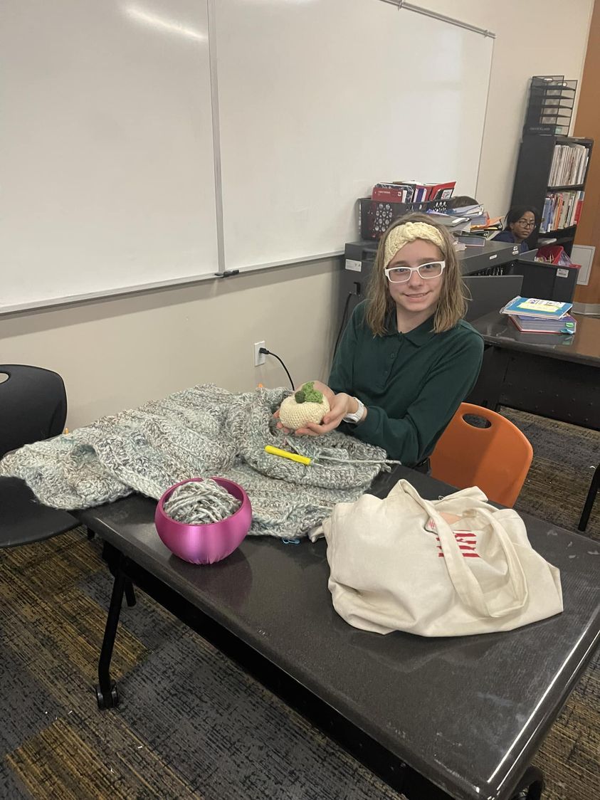 Student crocheting a blanket in Mrs. Cramers fiber arts true exploratory. She is wearing the headband she made and hol…